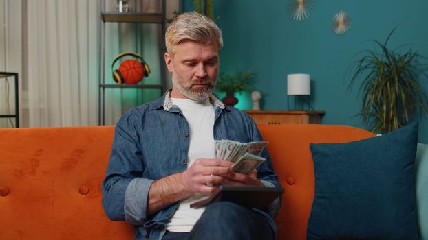 Planning budget. Rich middle-aged man counting money cash use calculator and calculate domestic bills at home. Senior old guy satisfied of income earnings, win, saves money for planned vacation, gifts