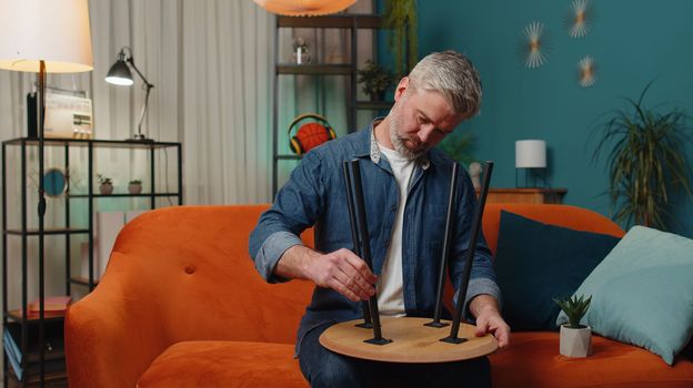 Happy bearded man finishing assembling furniture at home. Successful table desk collect, repair, fixing. Guy after moving into new apartment. Advertisement of a furniture store. Mortgage, lifestyle