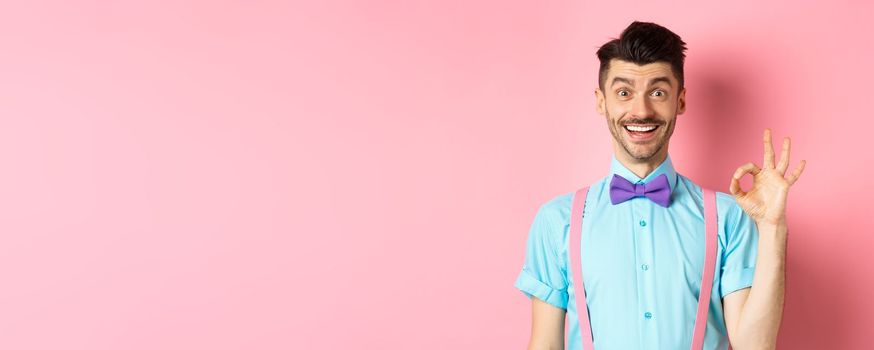 Handsome caucasian man with moustache smiling and showing okay sign, approve something good, praising excellent choice, standing amused on pink background.