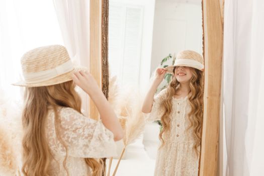 A beautiful teenage girl with long hair measures a straw hat in front of a mirror. Self-admiration of a blonde. selective focus