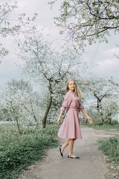 Blonde girl on a spring walk in the garden with cherry blossoms. Female portrait, close-up. A girl in a pink polka dot dress