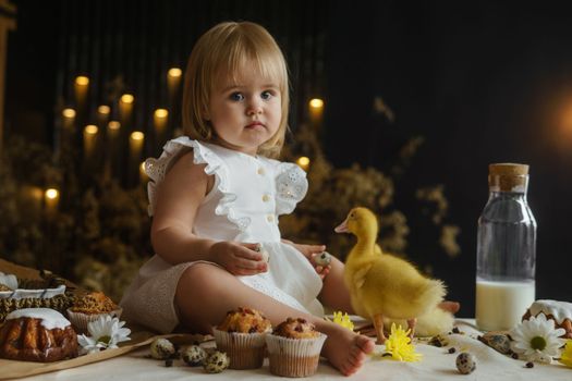 A little girl is sitting on the Easter table and playing with cute fluffy ducklings. The concept of celebrating happy Easter