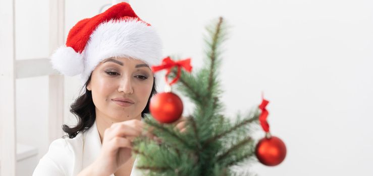 Portrait of smiling latin or indian business woman decorating christmas tree in office. Happy middle eastern woman decorating tree for christmas holiday. Multiethnic people celebrating holiday work.