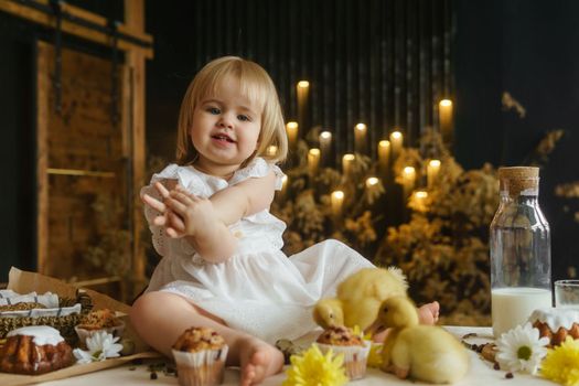 A little girl is sitting on the Easter table and playing with cute fluffy ducklings. The concept of celebrating happy Easter