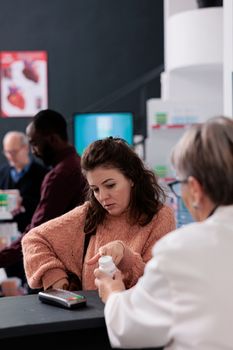 Portrait of caucasian cllient standing at pharmacy counter discussing health care treatment with pharmacist, wanting to buy cardiology pills. Drugstore employee offering medicine service and support