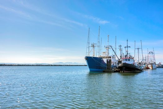 Small fishing trawler and tugboat moored at the ocean pier on blue sky background