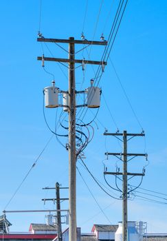 Electric posts and power transmission line, wooden electricty pole with mounted transformators on blue sky background