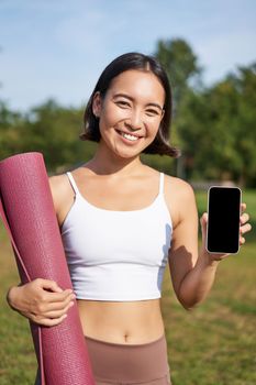 Vertical shot of fit and healthy young asian woman, shows smartphone screen with her workout stats, recommends telephone application.
