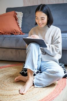 Vertical shot of cute asian girl in cozy home, drawing on her digital tablet with pen, designer working on project.