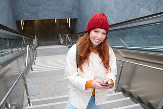 Smiling girl walking on stairs, using mobile phone, texting message on her way, using smartphone app map, follows route to destination place.