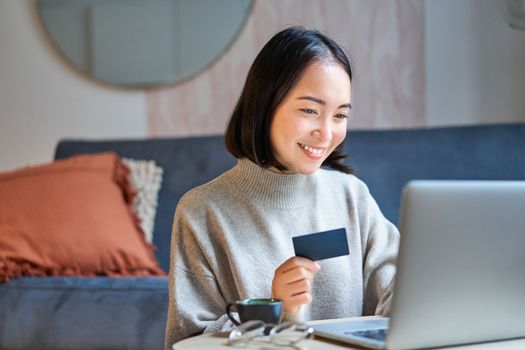 Portrait of korean woman shopping online, using her credit card and laptop to order delivery from website.