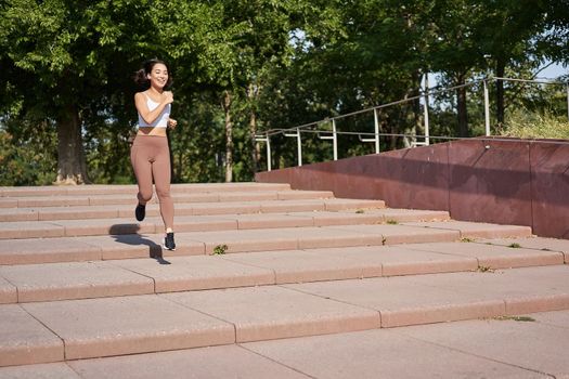 Healthy fitness girl running outdoors on street, wearing uniform, jogging on fresh air and listening music in wireless headphones.