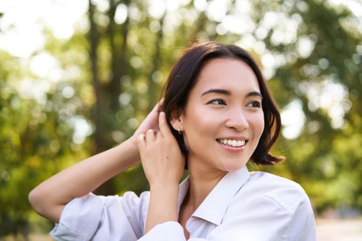 Women and beauty. Portrait of young happy asian woman walking on streets, enjoying stroll in park, smiling and looking around.