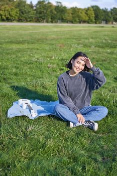 Beautiful asian girl, musician sitting in park and playing ukulele, smiling happy at camera. Lifestyle and young people concept.