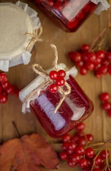 Viburnum fruit jam in a glass jar on a wooden table near the ripe red viburnum berries. Source of natural vitamins.