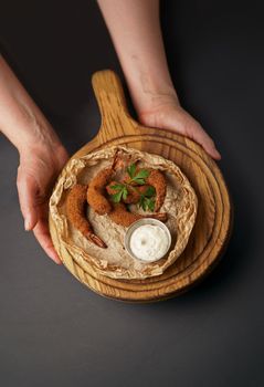 Shrimp in breadcrumbs and sauce isolated on a black background. Grilled shrimp on a board in the hands of a waiter.