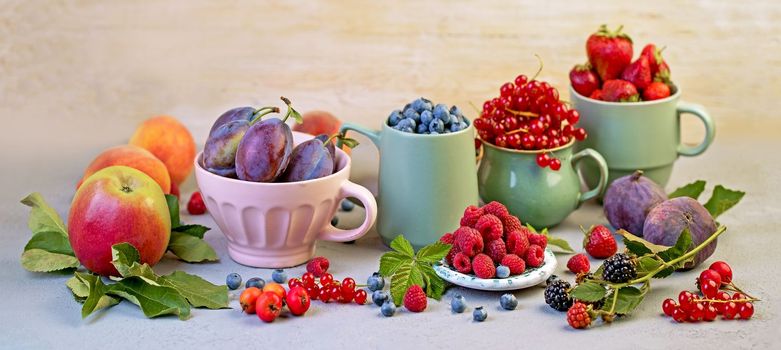 A variety of summer berries - raspberries, strawberries, blueberries, cherries, currants, plums - in cups on a wooden table