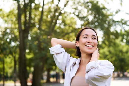 Women and beauty. Portrait of young happy asian woman walking on streets, enjoying stroll in park, smiling and looking around.