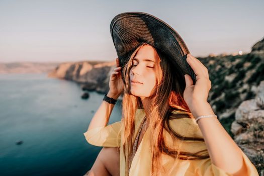 Portrait of happy young woman wearing summer black hat with large brim at beach on sunset. Closeup face of attractive girl with black straw hat. Happy young woman smiling and looking at camera at sea