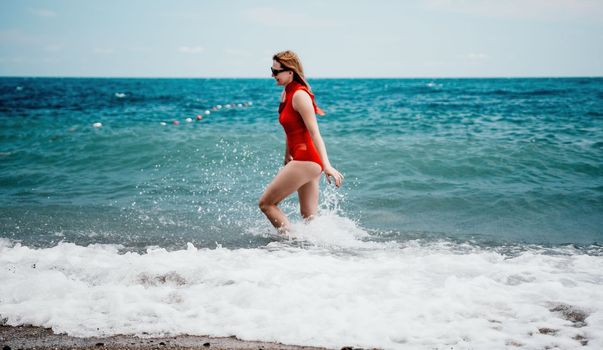 Young happy woman walks carefree on the seaside. Happy lady in red bikini. Portrait beautiful young woman relax smile around beach sea ocean in holiday vacation travel trip.