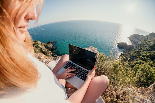 Woman sea laptop. Business woman in yellow hat working on laptop by sea. Close up on hands of pretty lady typing on computer outdoors summer day. Freelance, digital nomad, travel and holidays concept.