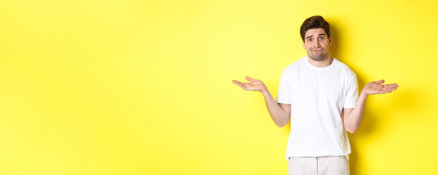 Clueless man in white t-shirt, shrugging and looking puzzled, dont know anything, standing over yellow background.