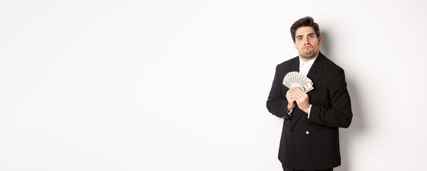 Image of greedy guy in black suit, holding money and unwilling to share, standing over white background.