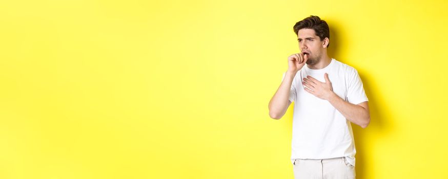Image of man with covid-19 or flu symptoms, coughing and feeling sick, standing over yellow background. Copy space