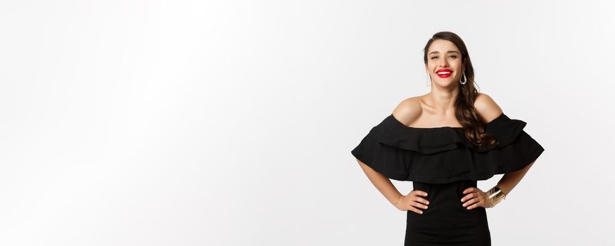 Beauty and fashion concept. Elegant young woman wearing party dress and red lipstick, laughing at camera, standing cheerful against white background.