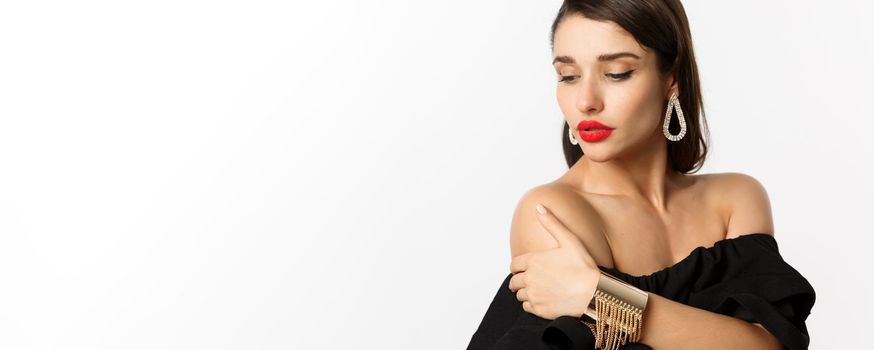 Fashion and beauty concept. Elegant woman with red lips, black dress, showing earrings and jewelry, white background.