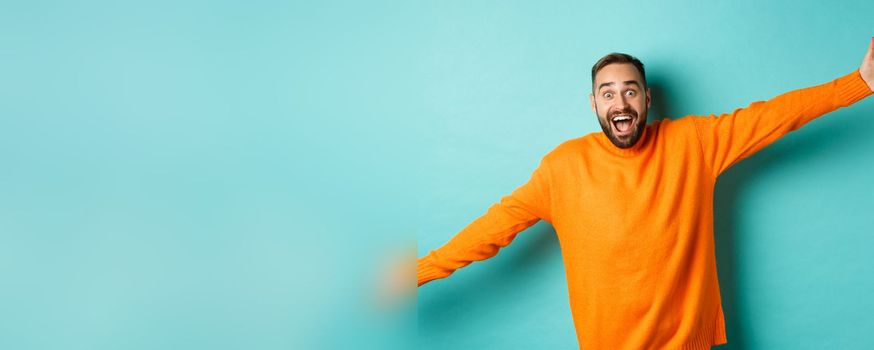 Surprised and happy man spread hands in warm welcome, reaching for hug, greeting you, showing something big, standing over light blue background.