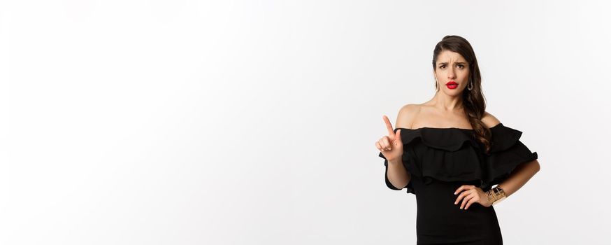 Fashion and beauty. Sassy woman in black dress saying no, disagree and shaking finger displeased, rejecting offer, declining something, standing over white background.