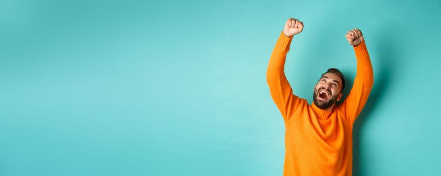 Happy man triumphing and feeling rejoice of winning, celebrating victory, standing over light blue background. Copy space