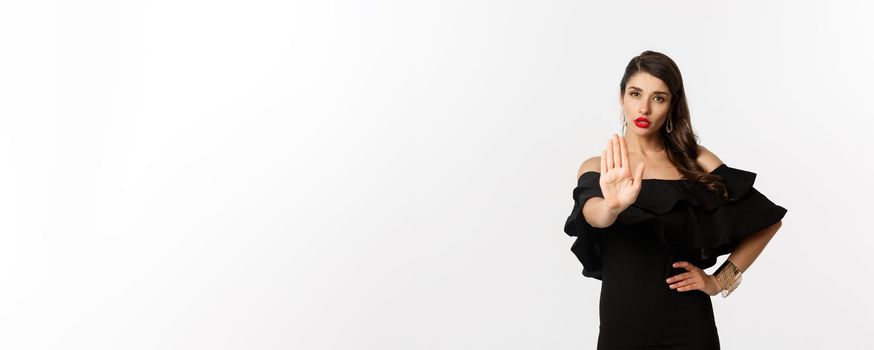Fashion and beauty. Confident attractive woman telling no, showing stop gesture and looking serious at camera, disapprove and prohibit, standing over white background.