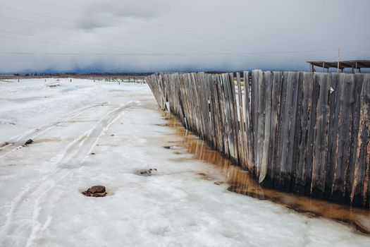 The old fence sinks in the melted snow in the fog of a remote village