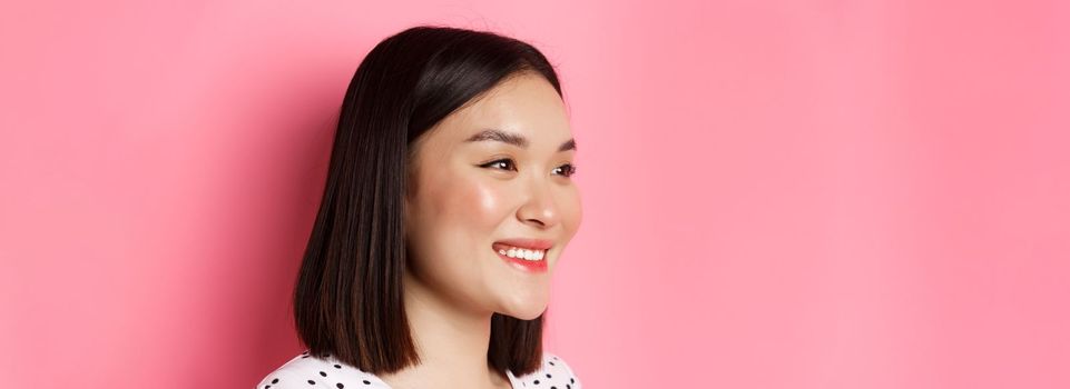 Beauty and skin care concept. Profile of beautiful asian girl smiling and looking happy left, standing against pink background.