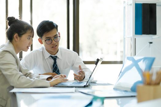 Businesspeople or office workers are working together on investment project. They are discussing, sharing the ideas, planning, and analyzing the business strategy. And set up the budget for financial plan by using laptop and calculator.