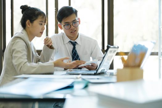 Businesspeople or office workers are working together on investment project. They are discussing, sharing the ideas, planning, and analyzing the business strategy. And set up the budget for financial plan by using laptop and calculator.