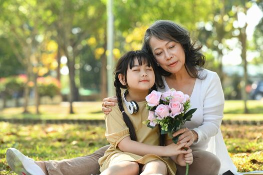 Cute little girl and grandmother holding bouquet of pink roses in hands, enjoying carefree leisure weekend together outdoor.