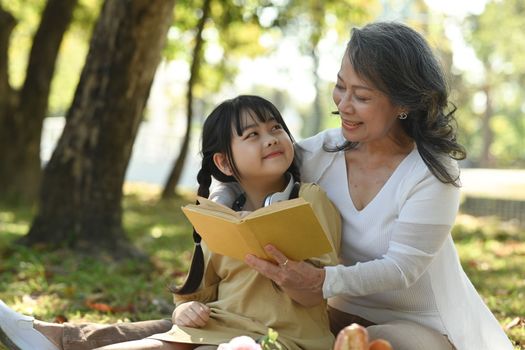 Image of loving grandmother embracing and reading fairytale to little grandchild. Family, generation and people concept.