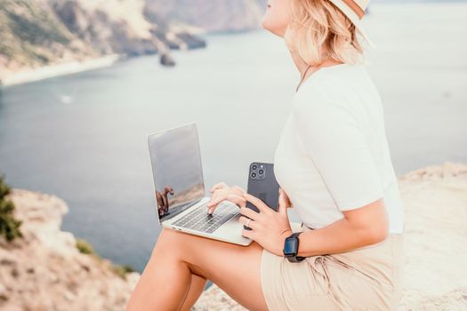 Digital nomad, Business woman working on laptop by the sea. Pretty lady typing on computer by the sea at sunset, makes a business transaction online from a distance. Freelance remote work on vacation