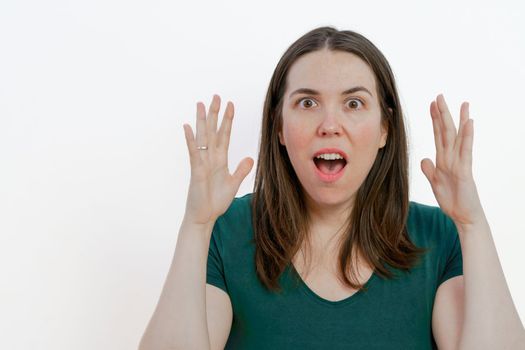 long-haired brunette woman with open mouth surprised looking at the camera with her arms raised white background
