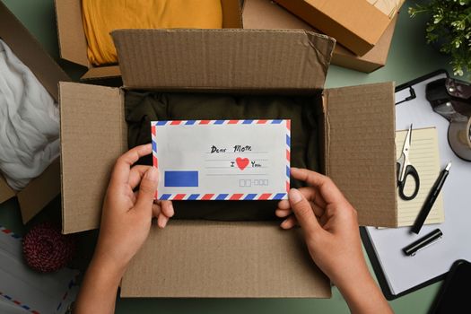 Above view of woman packing presents, putting greeting card into gift box for family during holiday season.