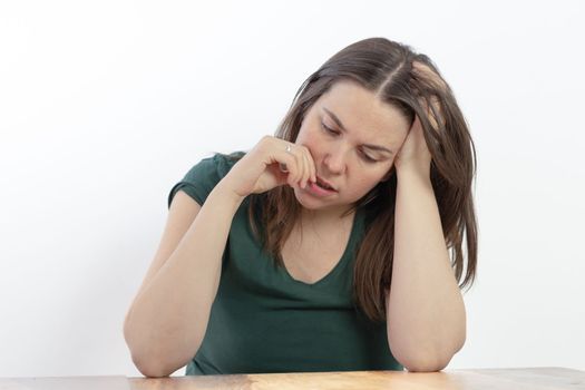 close-up of a young woman, brunette, long-haired, pensive looking at the ground with her finger in her mouth on a white background