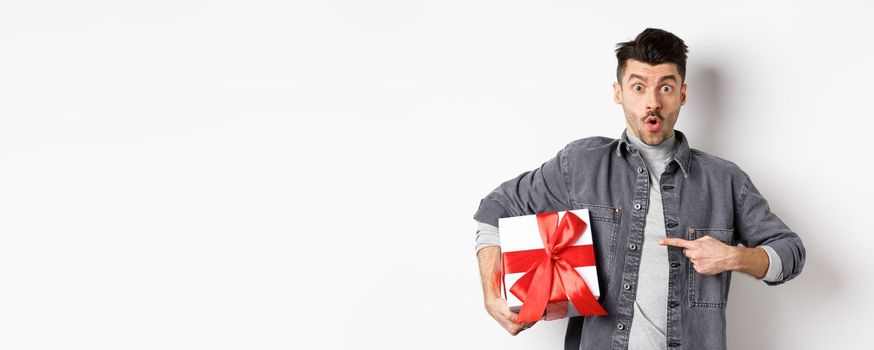 Happy Valentines day. Man shopping for romantic date, pointing at gift box and looking amazed, saying wow impressed, showing lover present, white background.