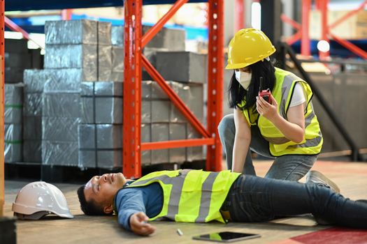 Warehouse worker lying unconscious on floor after accident while colleague calling for help or reporting work accident by walkie talkie.