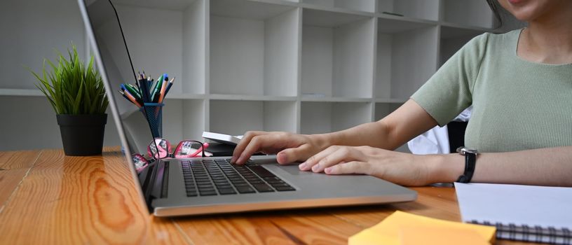 Close up young woman working with laptop computer on wooden desk.