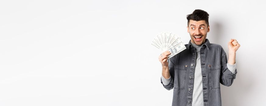Lucky man winning prize money and scream of excitement, staring at dollar bills happy, standing on white background.