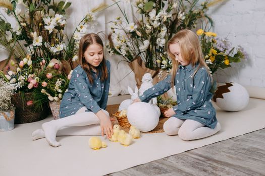 Two girls in a beautiful Easter photo zone with flowers, eggs, chickens and Easter bunnies. Happy Easter holiday