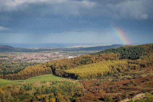 View from the summit of Roseberry Topping, Yorkshires Matterhorn, with a rainbow arcing over Guisborough under a moody sky, North York Moors National Park, UK